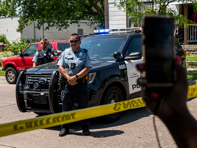 A woman holds up her phone as Minneapolis Police officers respond at a crime scene on June