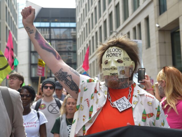LONDON, UNITED KINGDOM - 2021/08/27: Extinction Rebellion activist with a mask seen gesturing in City of London financial district during Blood Money March. Extinction Rebellion activists threw red paint and glued themselves to financial district buildings during the protest. The demonstrators "Demand change to the oppressive colonial system that drives …