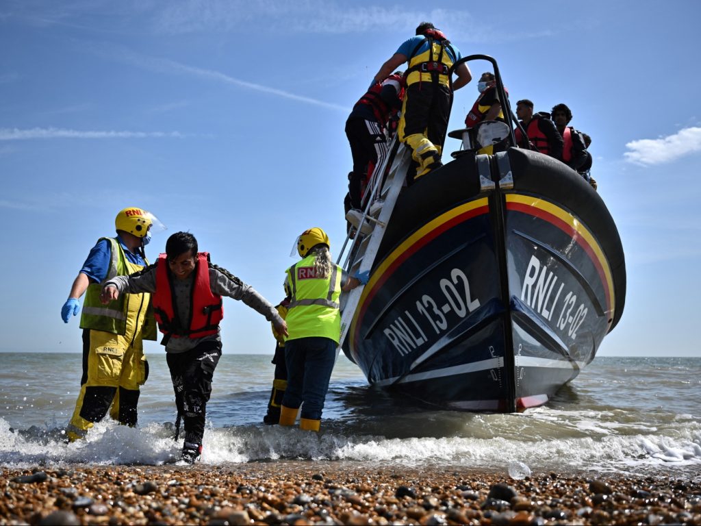 Royal National Lifeboat Institution's (RNLI) members of staff help migrants to disembark from one of their lifeboat after they were picked up at sea while attempting to cross the English Channel, on the beach of Dungeness, on the southeast coast of England, on June 15, 2022. - Furious Conservatives called on Britain's government on June 15, 2022 to abandon a European human rights pact after a judge dramatically blocked its plan to fly asylum-seekers to Rwanda. Under the UK's agreement with Rwanda, all migrants arriving illegally in Britain are liable to be sent to the East African nation thousands of miles away for processing and settlement. The government, after arguing that Brexit would lead to tighter borders, says the plan is needed to deter record numbers of migrants from making the perilous Channel crossing from northern France. (Photo by Ben Stansall / AFP) (Photo by BEN STANSALL/AFP via Getty Images)