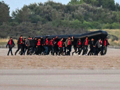 About fourty migrants, fom various origins, carry an inflatable boat towards the water bef