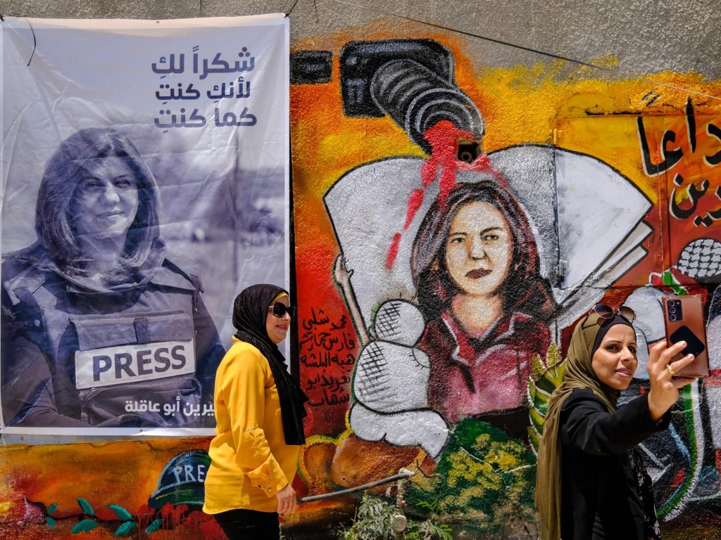 Palestinian women stand on May 19, 2022 in front of a mural, part of an art exhibit honouring slain Al-Jazeera journalist Shireen Abu Akleh (portraits), at the spot where she was killed on May 11 while covering an Israeli army raid in Jenin in the occupied West Bank. (Photo by RONALDO SCHEMIDT / AFP) (Photo by RONALDO SCHEMIDT/AFP via Getty Images)