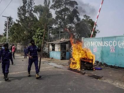 Congolese policemen walk past a fire set in front of United Nations Mission for the Stabil