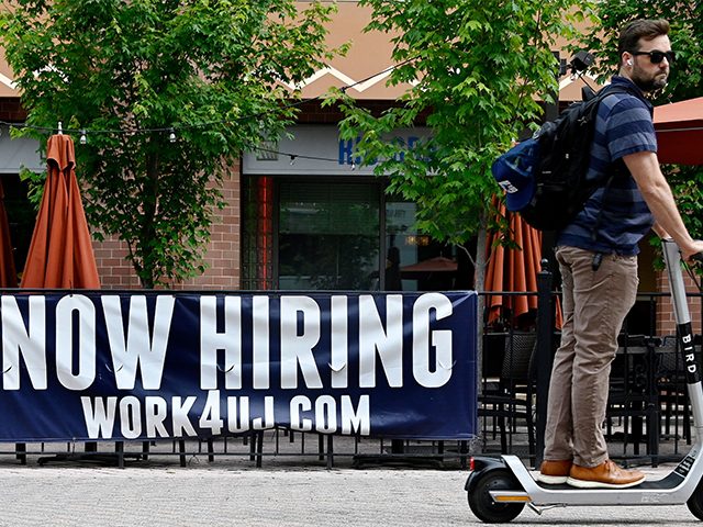 A man riding a scooter passes in front of a "now hiring" sign posted outside of a restaurant in Arlington, Virginia on June 3, 2022. - US employers added 390,000 jobs last month, the government reported on June 3, 2022, a sign of a slowdown in hiring but still a …