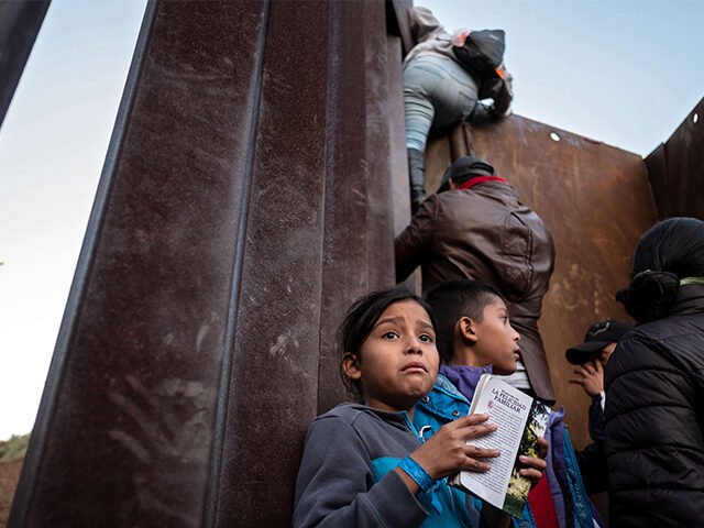 A Central American migrant girl holds a book as other migrants travelling in a caravan, climb the Mexico-US border fence in an attempt to cross to San Diego County, in Playas de Tijuana, Baja California state, Mexico on December 12, 2018. - Thousands of Central American migrants have trekked for …