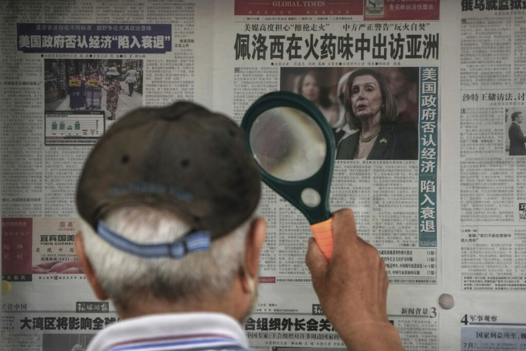 A man uses a magnifying glass to read a newspaper headline reporting on U.S. House Speaker Nancy Pelosi's Asia visit, at a stand in Beijing, Sunday, July 31, 2022. Pelosi, confirmed Sunday she will visit four Asian countries this week but made no mention of a possible stop in Taiwan that has fueled tension with Beijing, which claims the island democracy as its own territory. (AP Photo/Andy Wong)