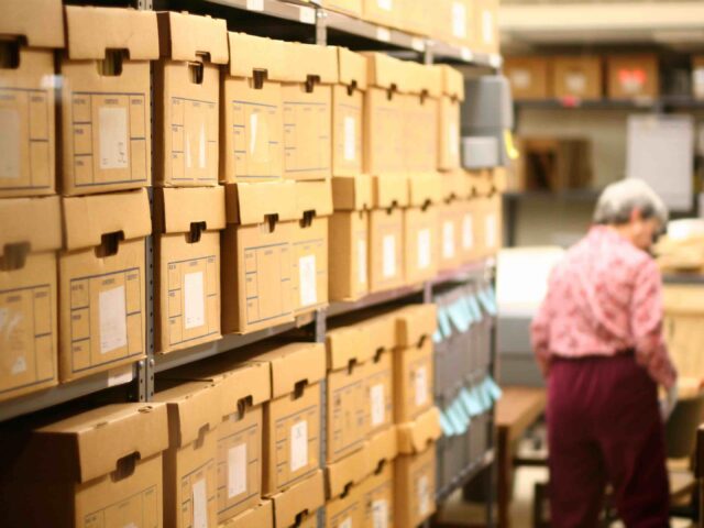 An elderly lady stands near the back of a record room at a library. (Getty)