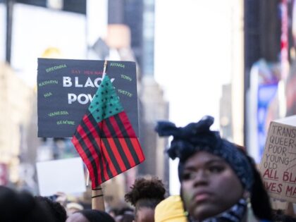 A protester holds a sign that say, "Black Power" with the names of women that have died at the hands of police with an American Flag that has been changed to the colors of Red, Black and Green in Times Square New York in support of Black Women. On July …
