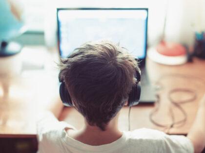 Little dependent gamer kid playing on laptop - stock photo