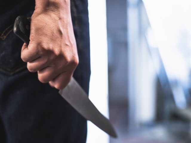 image of a robbers hands holding a knife in the shadows.