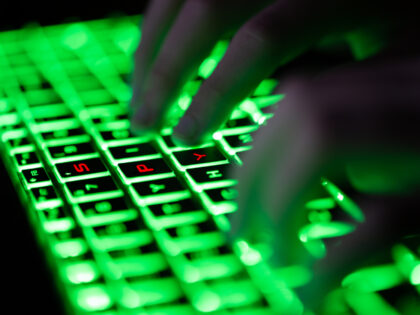 Digital composite of glowing green keyboard in the dark, the hands of a computer hacker typing and letters "SPY" in red on the keyboard