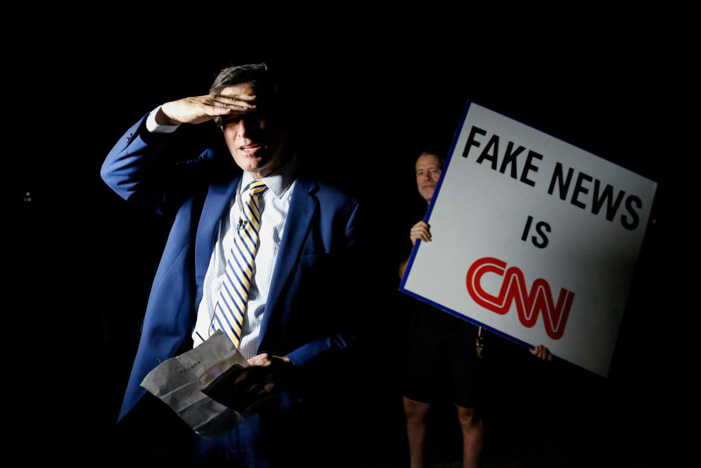 A man holding a sign that reads Fake News is CNN stands next to Michael Williams, an anchor of Channel 5 WPTV 
