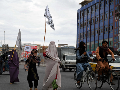 Afghan burqa-clad women carry flags as they walk along a street to celebrate the Taliban's victory in Kandahar on August 15, 2022. - Taliban fighters chanted victory slogans next to the US embassy in Kabul on August 15 as they marked the first anniversary of their return to power in …