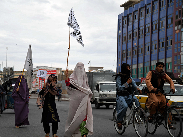 Afghan burqa-clad women carry flags as they walk along a street to celebrate the Taliban's