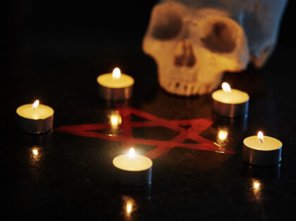 Five candles arranged at the apexes of a hand-drawn pentangle on a reflective stone surface, with a human skull.