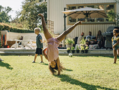 Girl doing cartwheel while playing with friends in backyard on sunny day