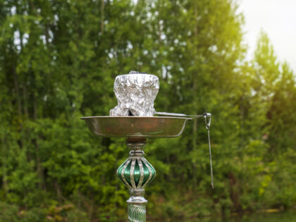 A green hookah in close-up stands on the bank of a river in the forest. The concept of outdoor recreation.