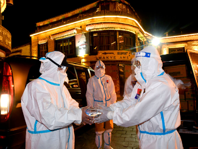 LHASA, CHINA - AUGUST 14: A volunteer gives out anti-epidemic supplies to an epidemic prevention worker on August 14, 2022 in Lhasa, Tibet Autonomous Region of China. Lhasa will extend disinfection work in its main urban areas until 3 a.m. on Thursday. (Photo by Li Lin/China News Service via Getty Images)