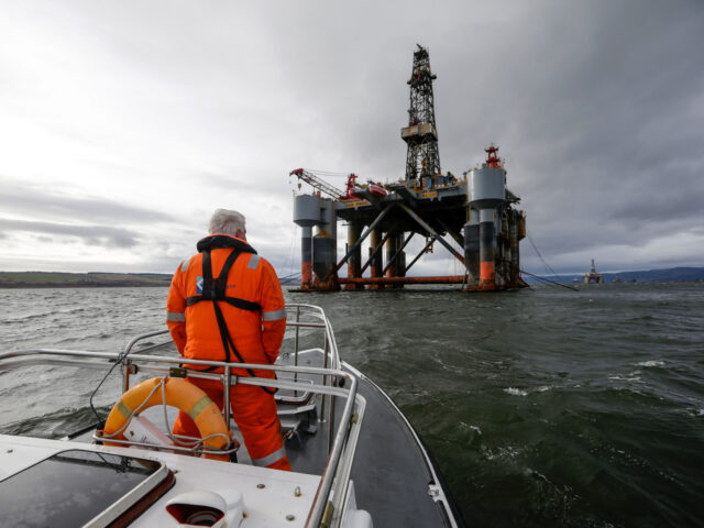 An employee stands on the deck of a pilot boat in view of the Ocean Princess oil platform,