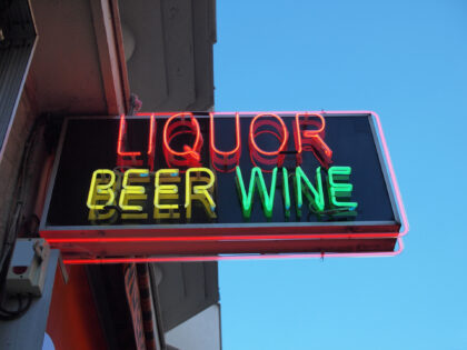 A neon sign on a store selling alcohol. The words, liquor, beer and wine glowing in bright neon. A clear blue sky in the background.