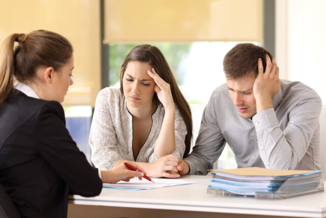 Saleswoman explaining conditions of a document with bad news to a couple of worried custom