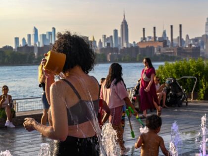 A woman pours water on her face to cool off in a fountain in Domino Park, Brooklyn with the Manhattan skyline in the background as the sun sets during a heat wave on July 24, 2022 in the Brooklyn borough of New York City. The five boroughs of New York …