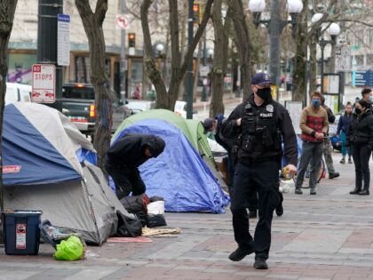 A Seattle Police officer walks past tents used by people experiencing homelessness, Friday, March 11, 2022, during the clearing and removal an encampment in Westlake Park in downtown Seattle. Mayor Bruce Harrell said Tuesday, May 31, 2022, that the city will create a database of homeless camps and provide more …