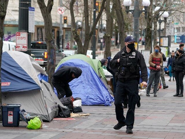 A Seattle Police officer walks past tents used by people experiencing homelessness, Friday