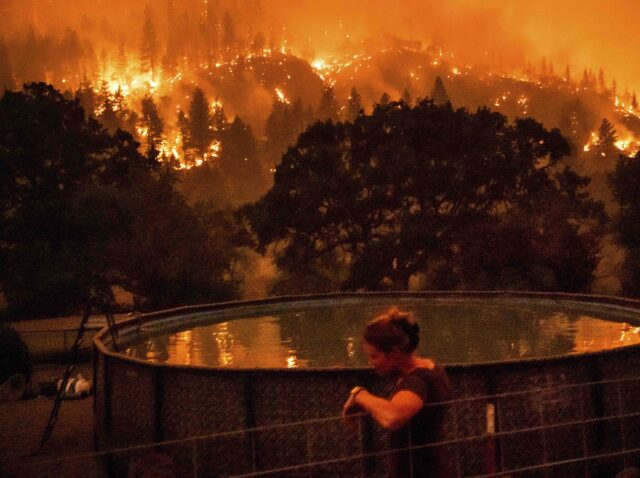 Angela Crawford leans against a fence as a wildfire called the McKinney fire burns a hills