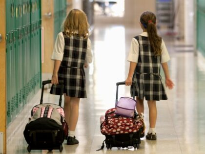 Eight year old girls head home after after school rolling their backpacks down the school hallway.