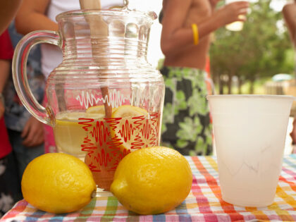 Jug, lemons and cups on lemonade stall, children (5-13) in background - stock photo