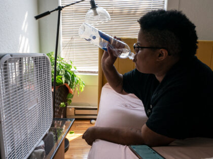 Katherine Morgan drinks water in front of a box fan while trying to stay cool in her downtown apartment without air conditioning on Thursday, Aug. 12, 2021, in Portland, Ore. People have headed to cooling centers as the Pacific Northwest began sweltering under another major, multiday heat wave. (AP Photo/Nathan …