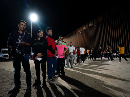 Migrants wait along a border wall Tuesday, Aug. 23, 2022, after crossing from Mexico near