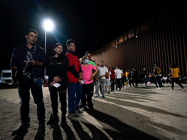 Migrants wait along a border wall Tuesday, Aug. 23, 2022, after crossing from Mexico near Yuma, Ariz. (AP Photo/Gregory Bull)