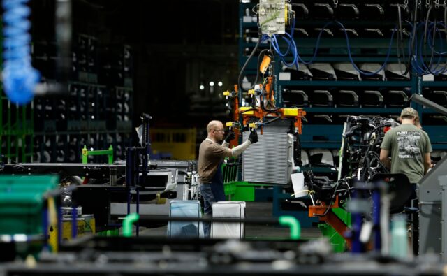 Line workers work on the chassis of full-size General Motors pickup trucks at the Flint As