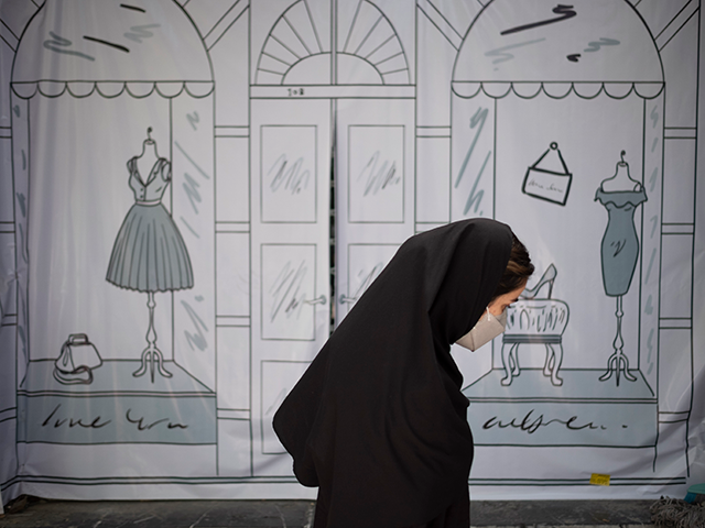 An Iranian woman walks past a shop window covered with a banner in northern Tehran on July 9, 2022. Iranian President Ebrahim Raisi in a meeting with officials on Wednesday called for non-compliance with hijab rules that promote corruption in an Islamic country like Iran.  (Photo by Morteza Nicobazel/NurPhoto from Getty Images)