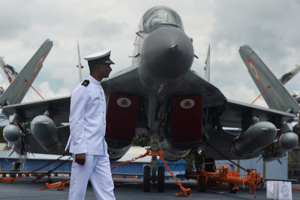 An Indian Navy officer walks past a Mig 29 fighter jet on the deck of the Indian indigenous aircraft carrier INS Vikrant during its commissioning at Cochin Shipyard in Kochi on September 2, 2022. - India debuted its first locally made aircraft carrier on September 2, a milestone in government efforts to reduce its dependence on foreign arms and counter China's growing military assertiveness in the region. (Photo by Arun SANKAR / AFP) (Photo by ARUN SANKAR/AFP via Getty Images)