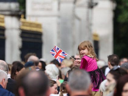 A Child sitting on the shoulders of an adult waves a Union Flag outside of Buckingham Pala