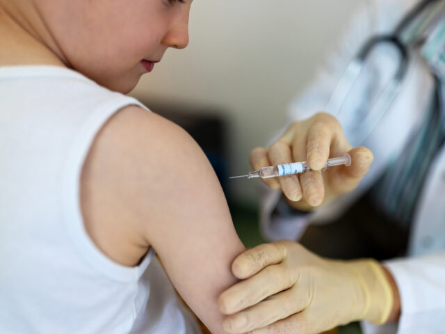 Boy getting a flu vaccine in the clinic. Small boy getting a vaccine on his arm by a pedia