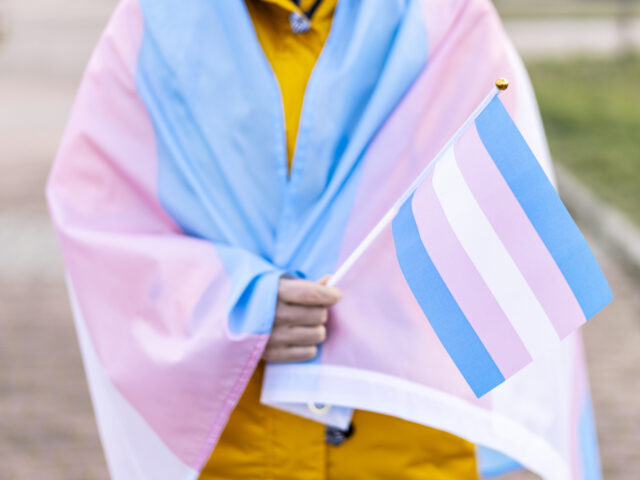 Transgender woman covered with the transgender flag and holding a flag in the hand for def