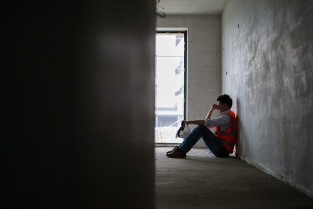 Depressed building contractor sitting inside incomplete house at construction site