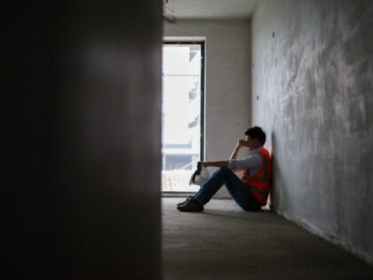 Depressed building contractor sitting inside incomplete house at construction site