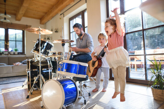 Portrait of happy small children with father indoors at home, playing drums.