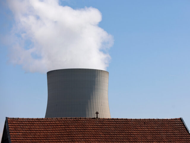 ESSENBACH, GERMANY - AUGUST 14: The Isar nuclear power plant, which includes the Isar 2 reactor, stands seen behind the roof of a residential house topped with a cross on August 14, 2022 in Essenbach, Germany. Isar 2 is one of the last three still operating nuclear power plants in …