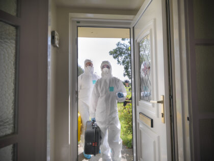 Forensic scientists entering house at crime scene, policeman in background