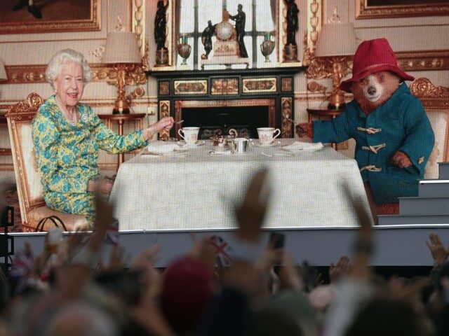The crowd watches a film of Queen Elizabeth II having tea with Paddington Bear on a big sc