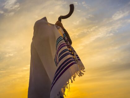 Man in a tallit, Jewish prayer shawl is blowing the shofar ram's horn (Getty)