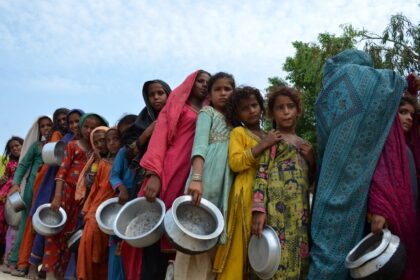 Displaced flood-affected people stand in a queue to receive food at a makeshift camp in fl
