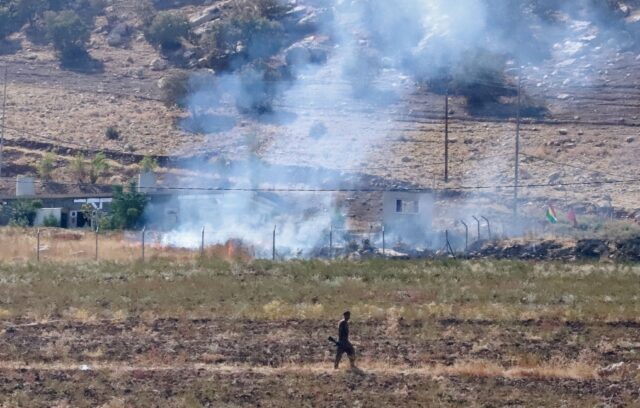 A Kurdish peshmerga fighter walks as smoke billows in the area of Zargwez, outside the Ira