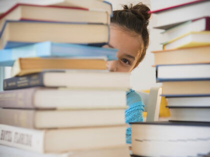 Girl peeking from behind stacks of books - stock photo