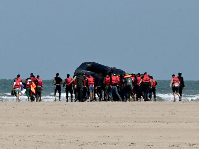 Migrants push an inflatable boat across a stretch of sand towards the water, near Gravelin